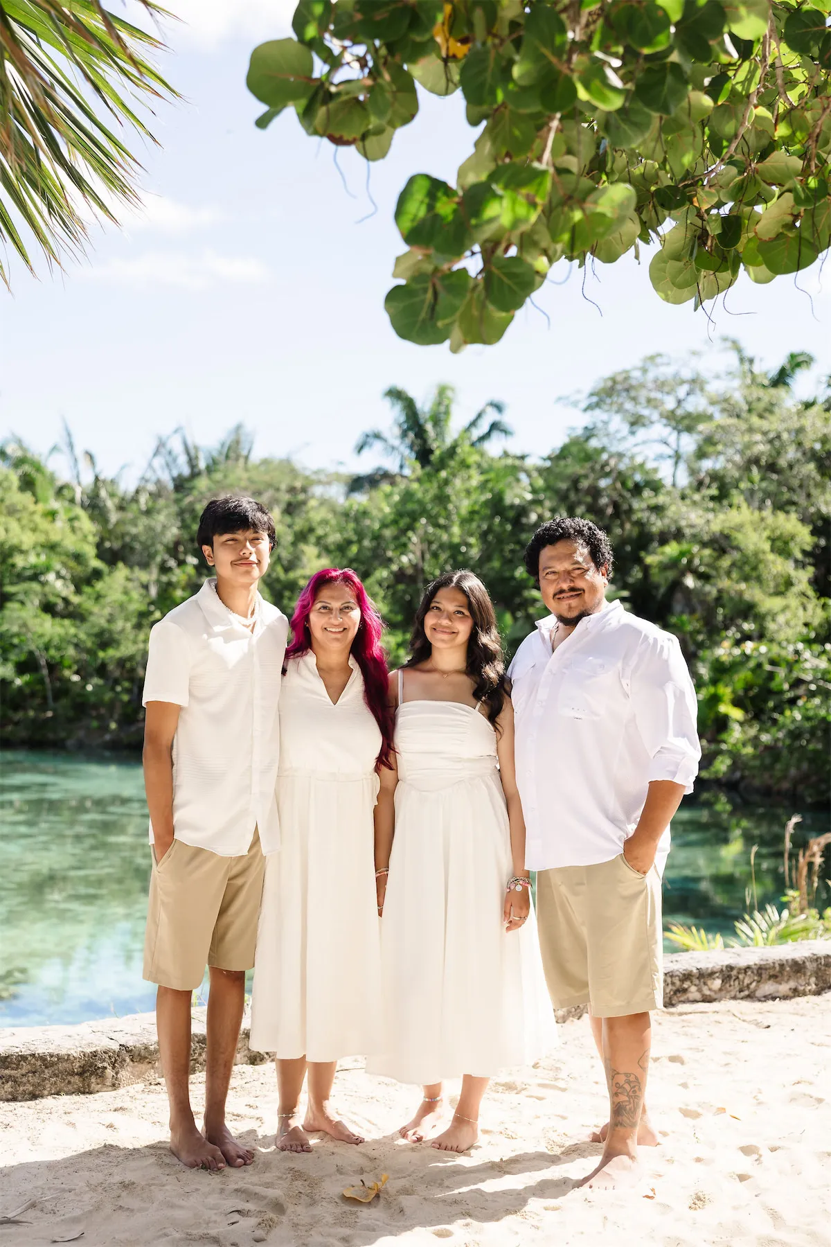 A family of four in coordinated white and khaki outfits posing by the tropical lagoon at Chankanaab Park in Cozumel, Mexico.