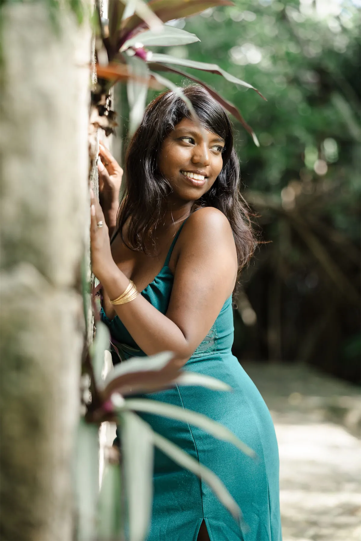 A woman in a green dress leaning against a stone wall in the lush botanical gardens of Chankanaab Park in Cozumel.