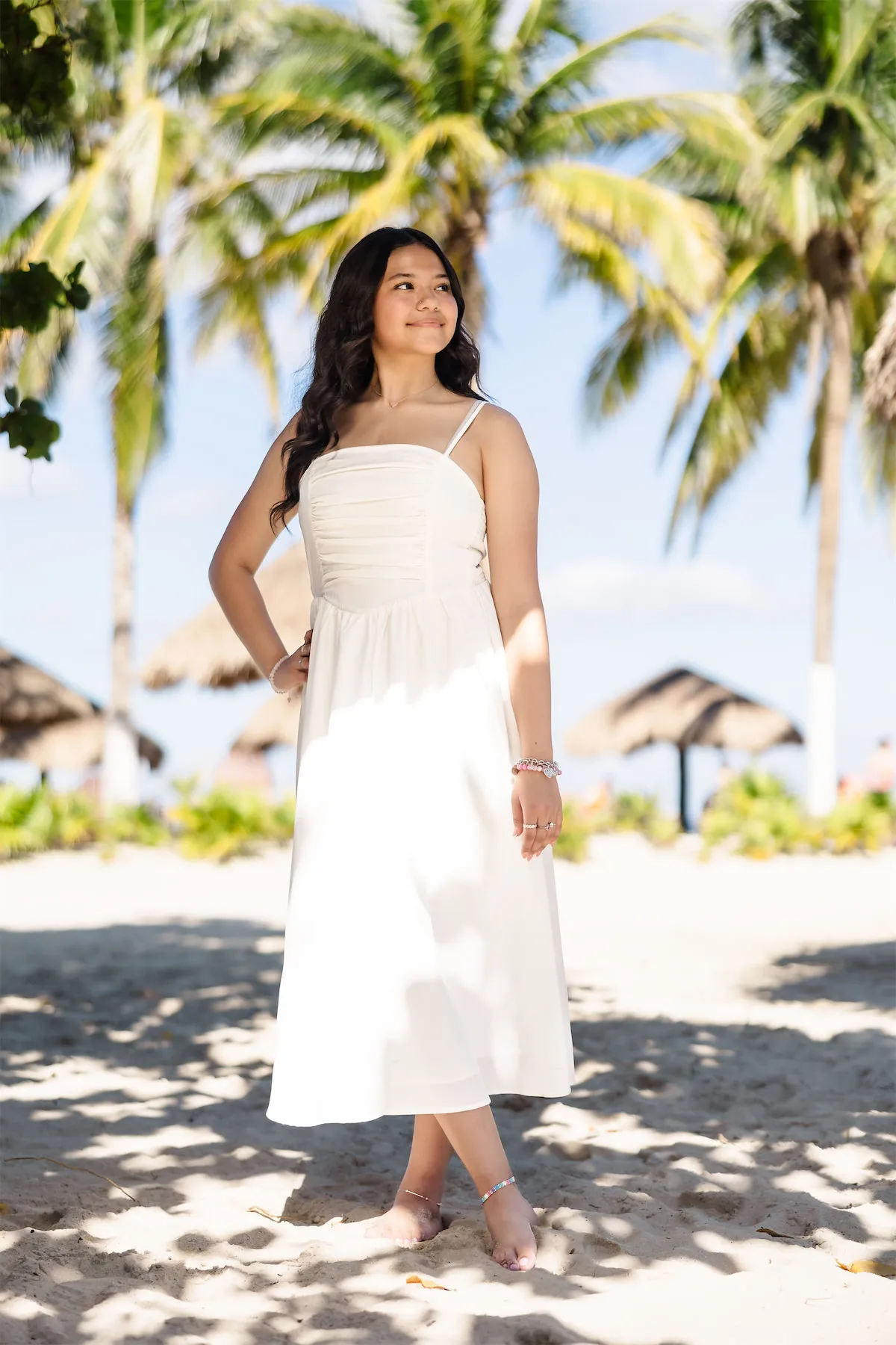A young woman in a white summer dress posing under palm trees at Chankanaab Park in Cozumel, Mexico.