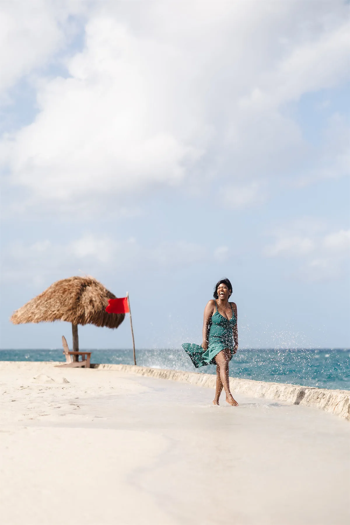 A happy woman in a green dress running through ocean spray on the beach at Chankanaab Park in Cozumel.