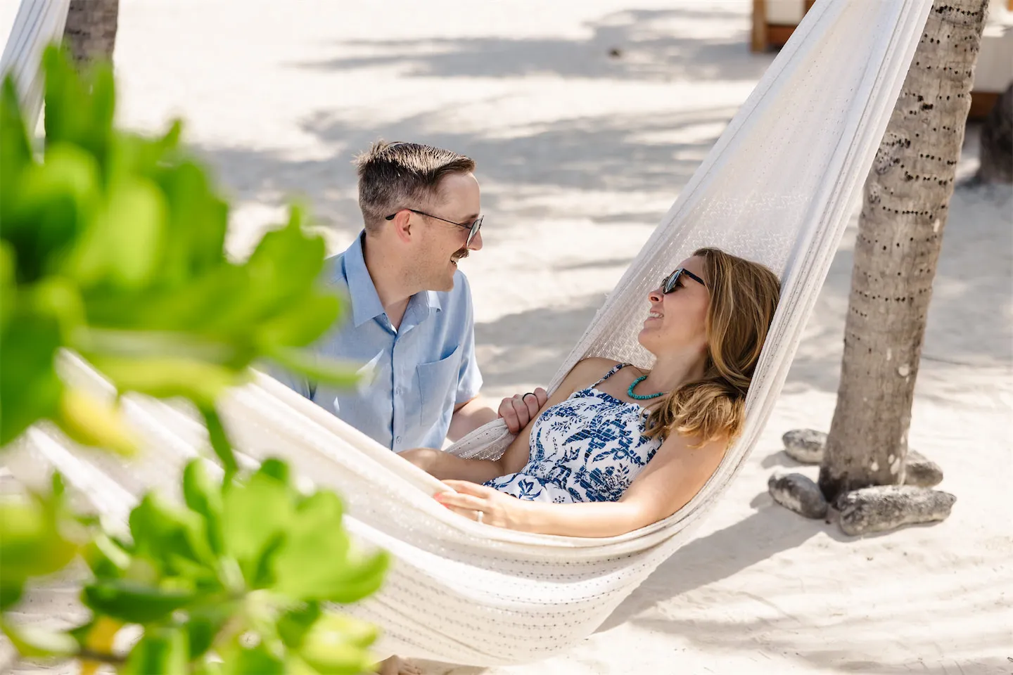 A couple laughing and sharing a candid moment in a white woven beach hammock in Cozumel.