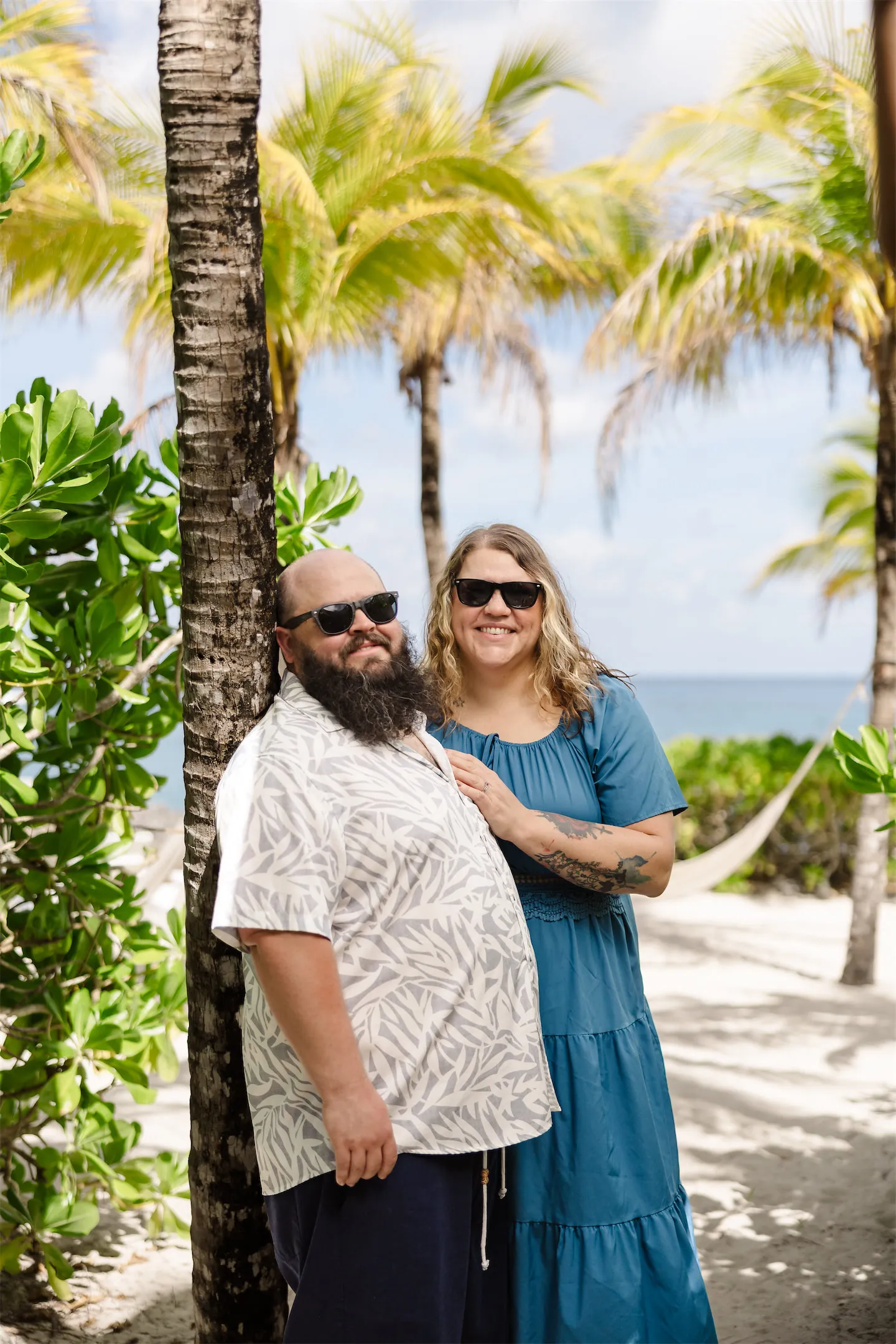 A couple posing by a palm tree at a tropical Cozumel beach club during a vacation photo session.