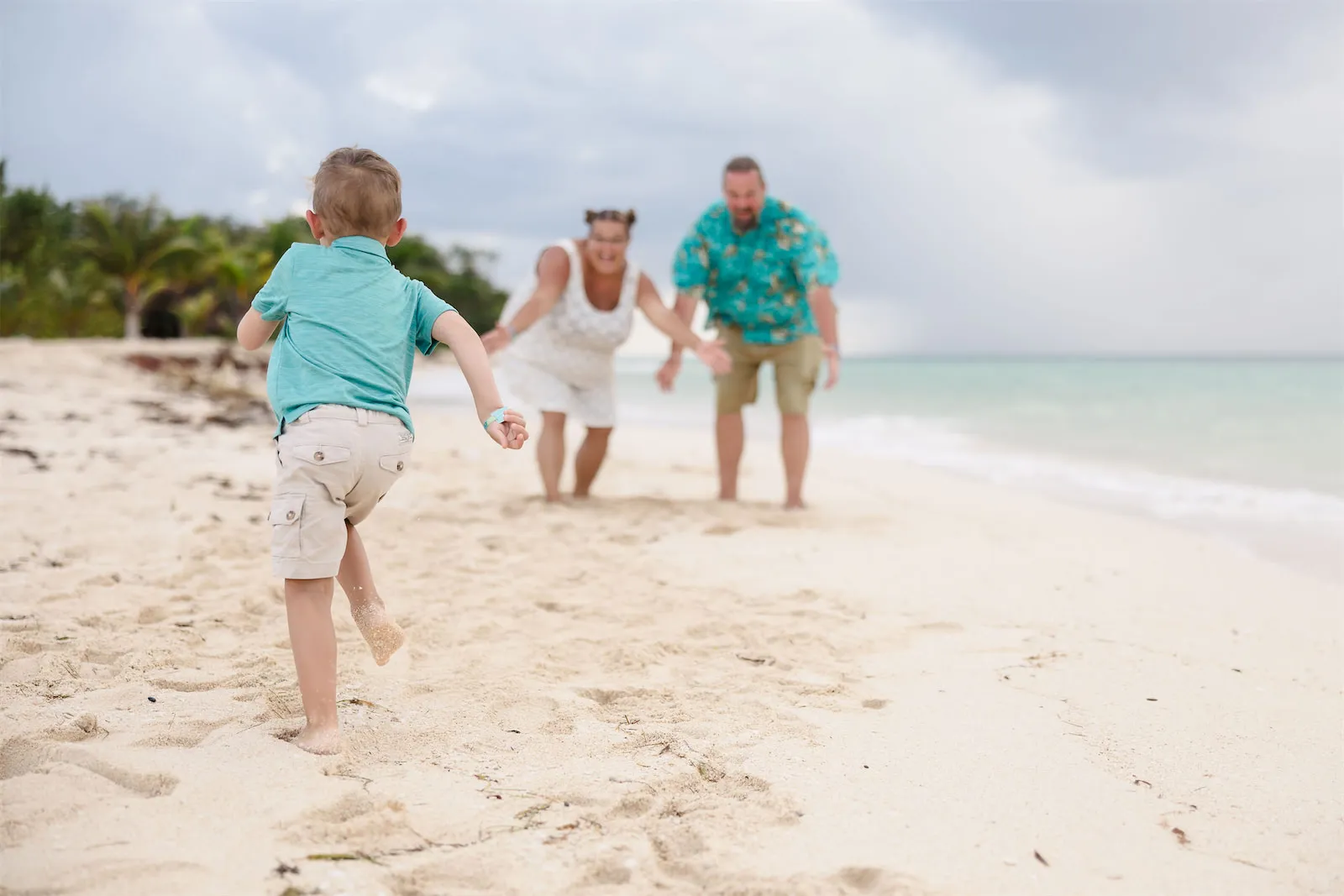 A young boy running toward his parents on a white sand beach in Cozumel, Mexico.