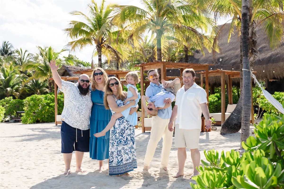 A group of friends and family laughing and posing candidly at a tropical beach club in Cozumel with palm trees and cabanas.