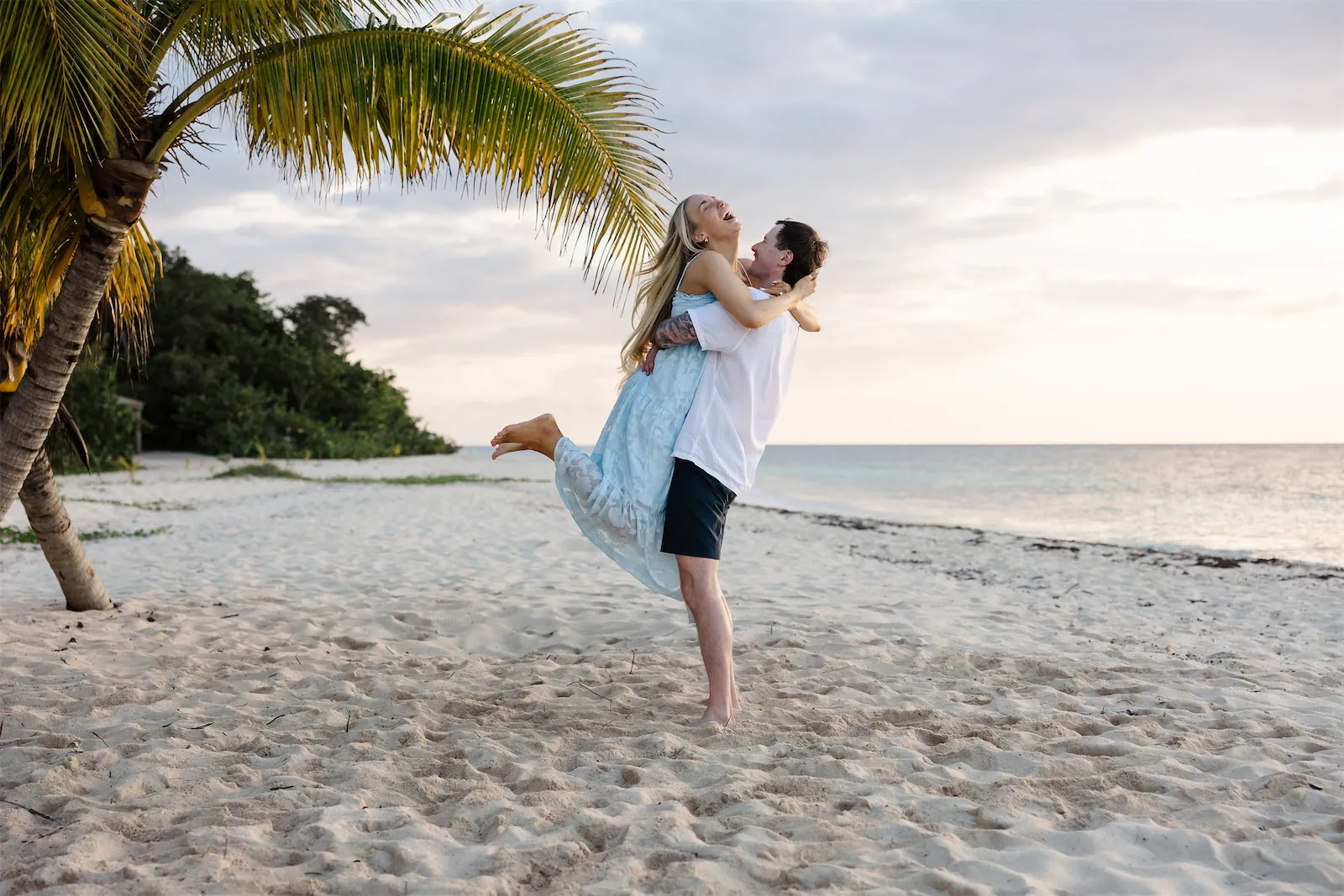 A man lifting and spinning his partner while laughing on a white sand beach in Cozumel, Mexico.