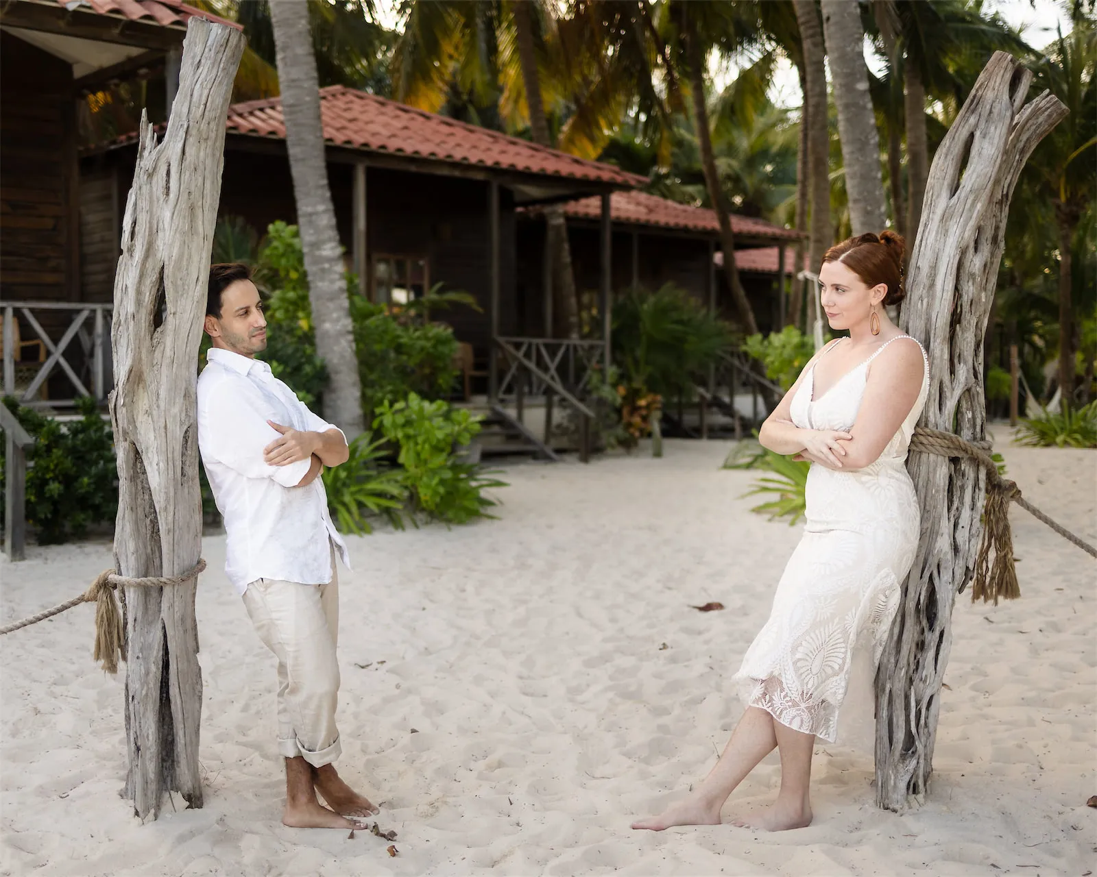 A man and woman leaning against weathered wooden posts on a sandy beach path in Cozumel, Mexico.