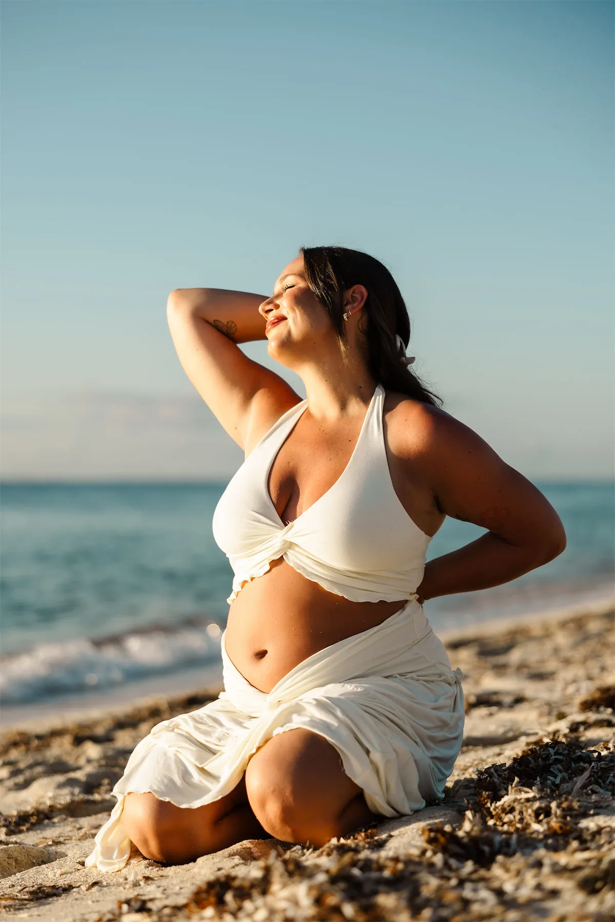 A glowing pregnant woman posing on the sand at sunset during a maternity photo session in Cozumel.