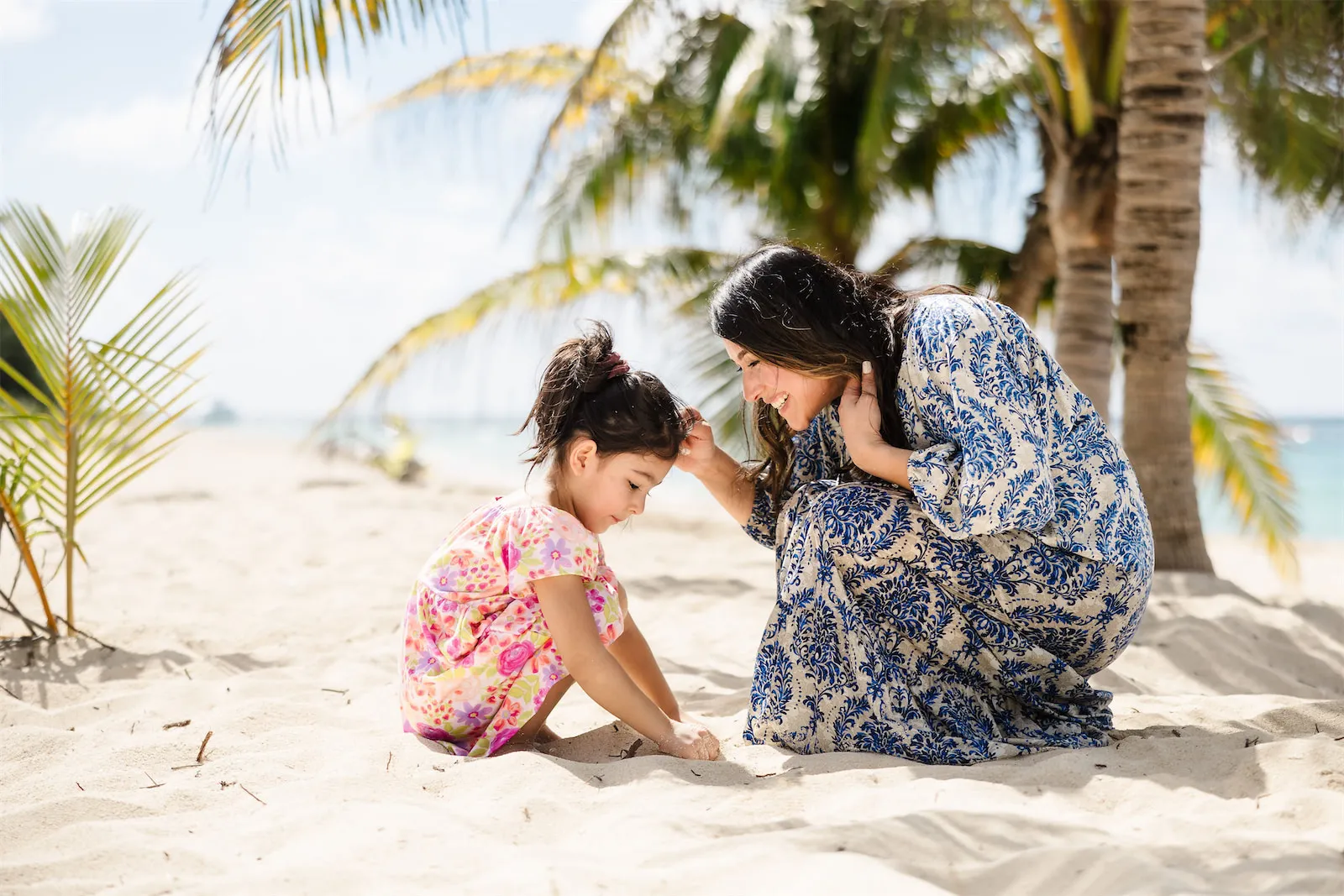 A mother and daughter playing in the sand together under palm trees on a Cozumel beach.