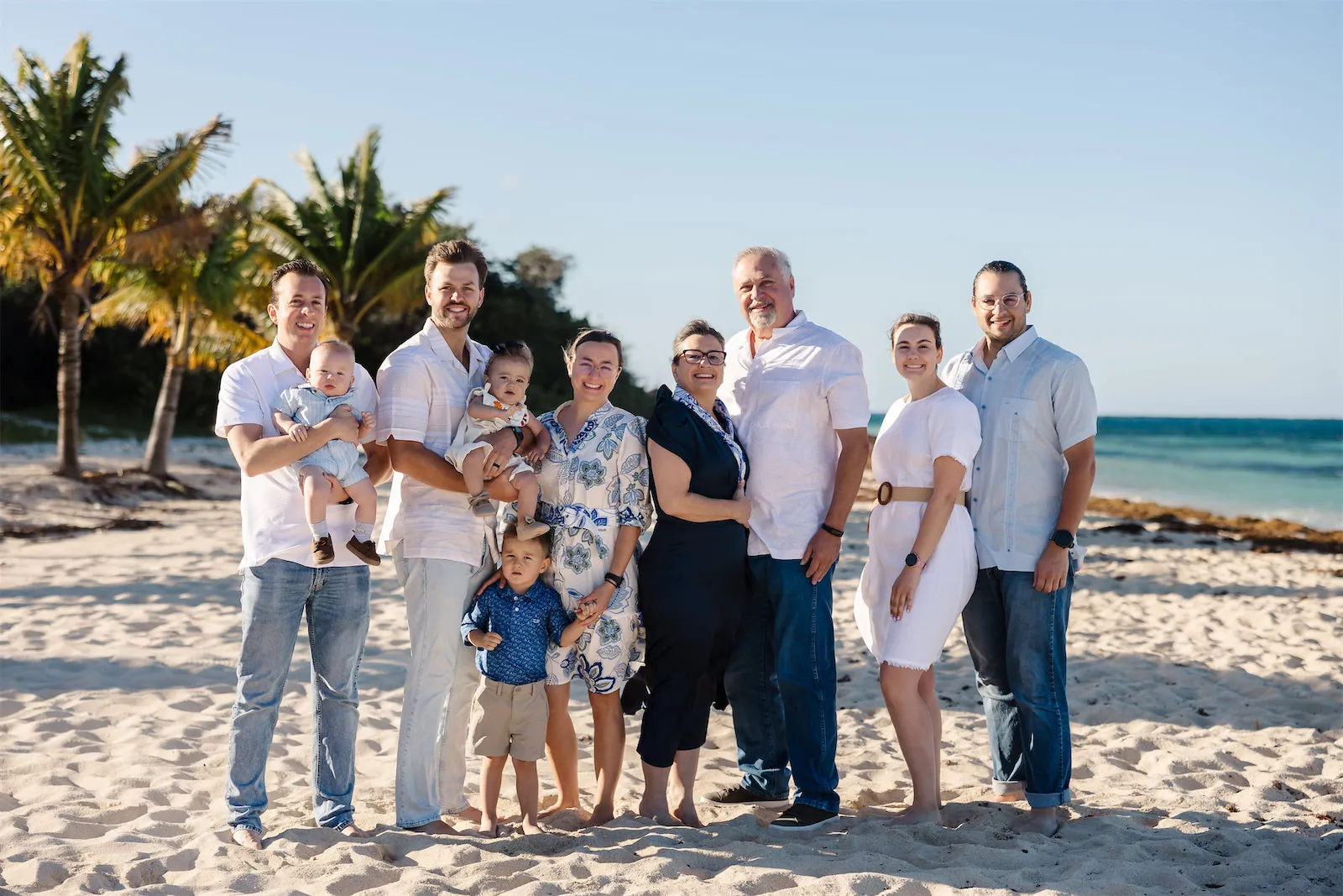 A large multigenerational family with infants and young children posing for a group portrait on a Cozumel beach.