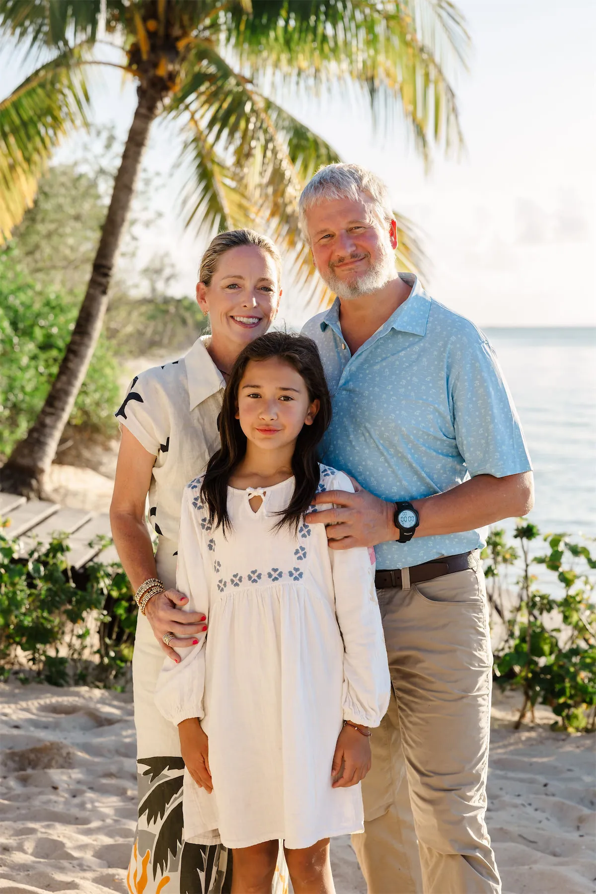 A family of three posing for a beach portrait under a palm tree at the Occidental Hotel in Cozumel during golden hour.