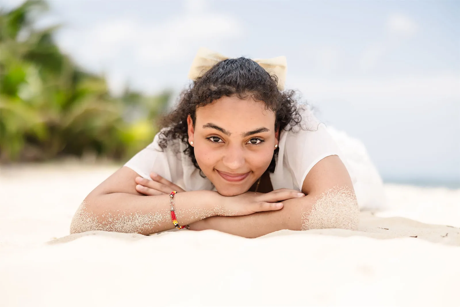 A young woman in a white dress smiling while lying on the sand at Paradise Beach in Cozumel, Mexico.