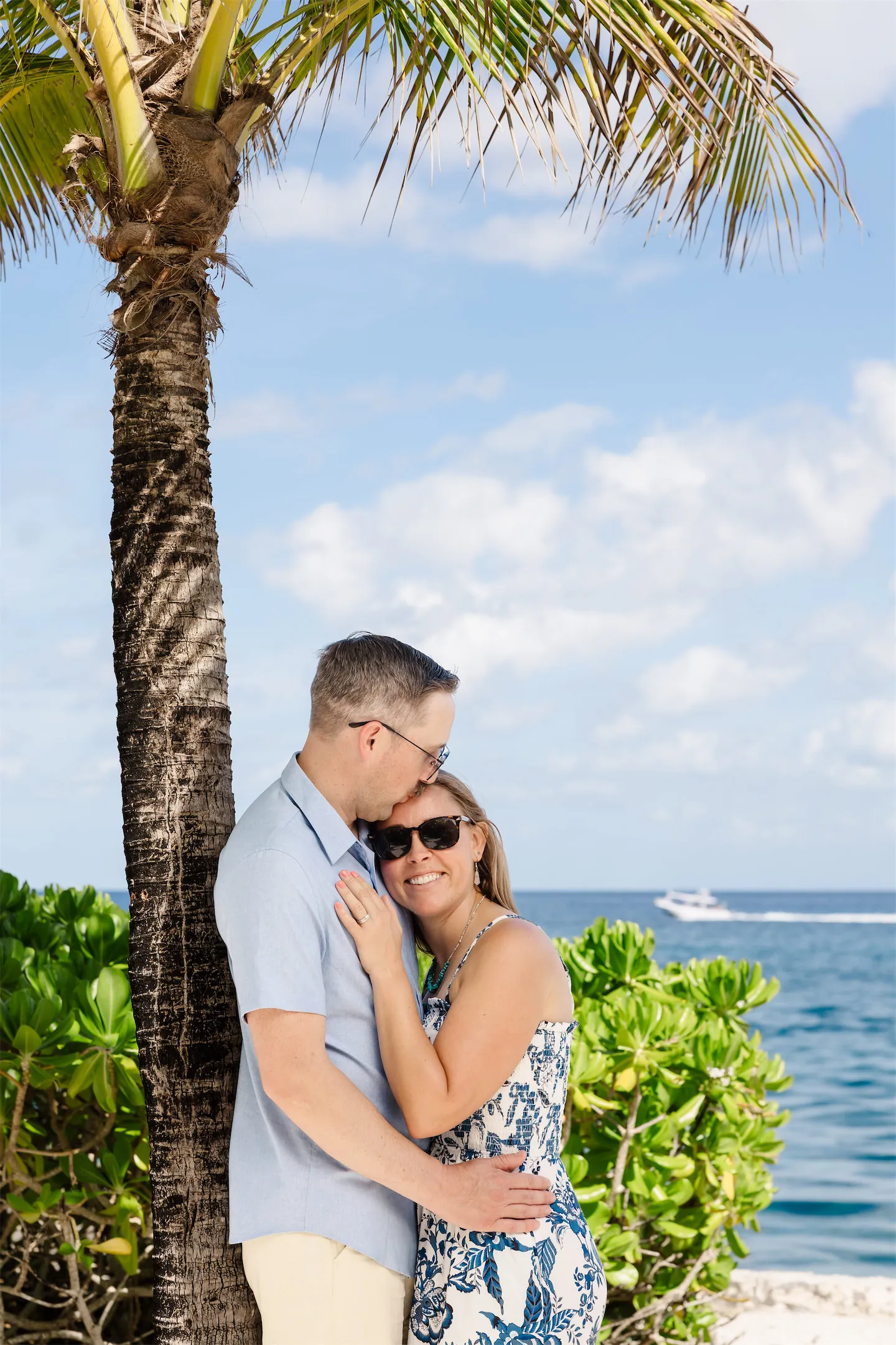 A couple posing romantically leaning against a palm tree with the turquoise Caribbean sea in the background of Cozumel.