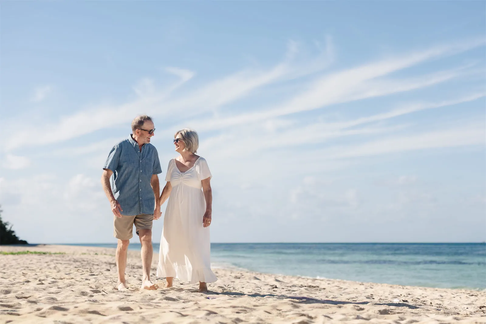 A happy senior couple holding hands and walking along a white sand beach during their Cozumel vacation.