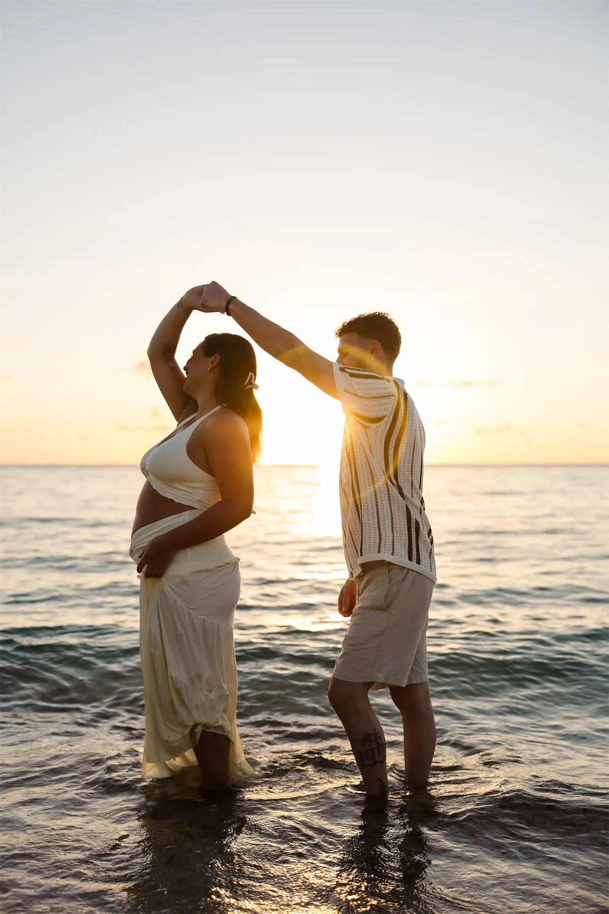 A couple dancing in the ocean waves during a golden hour maternity session in Cozumel.