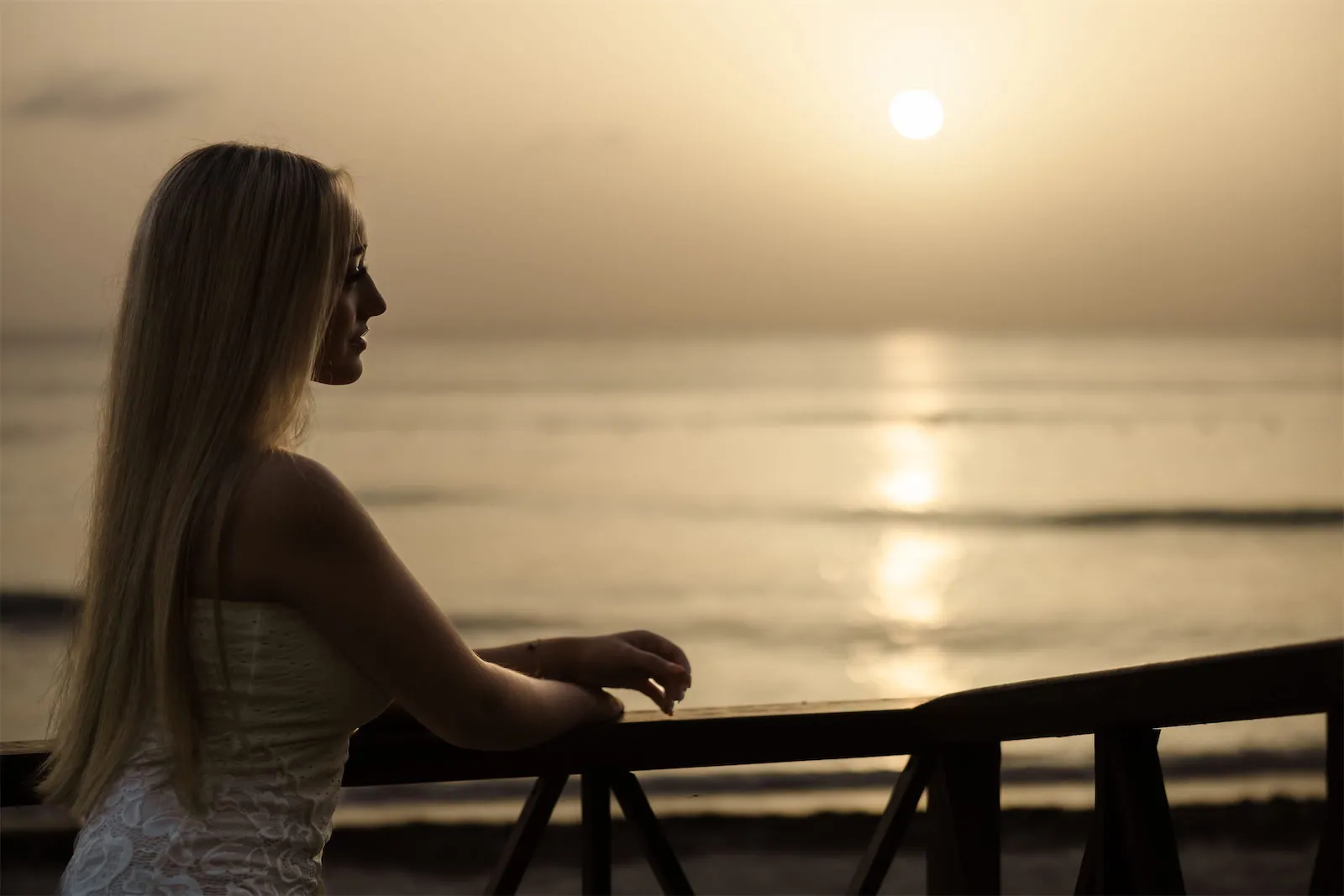 A profile silhouette of a blonde woman looking out at the ocean during a golden hour sunset in Cozumel.