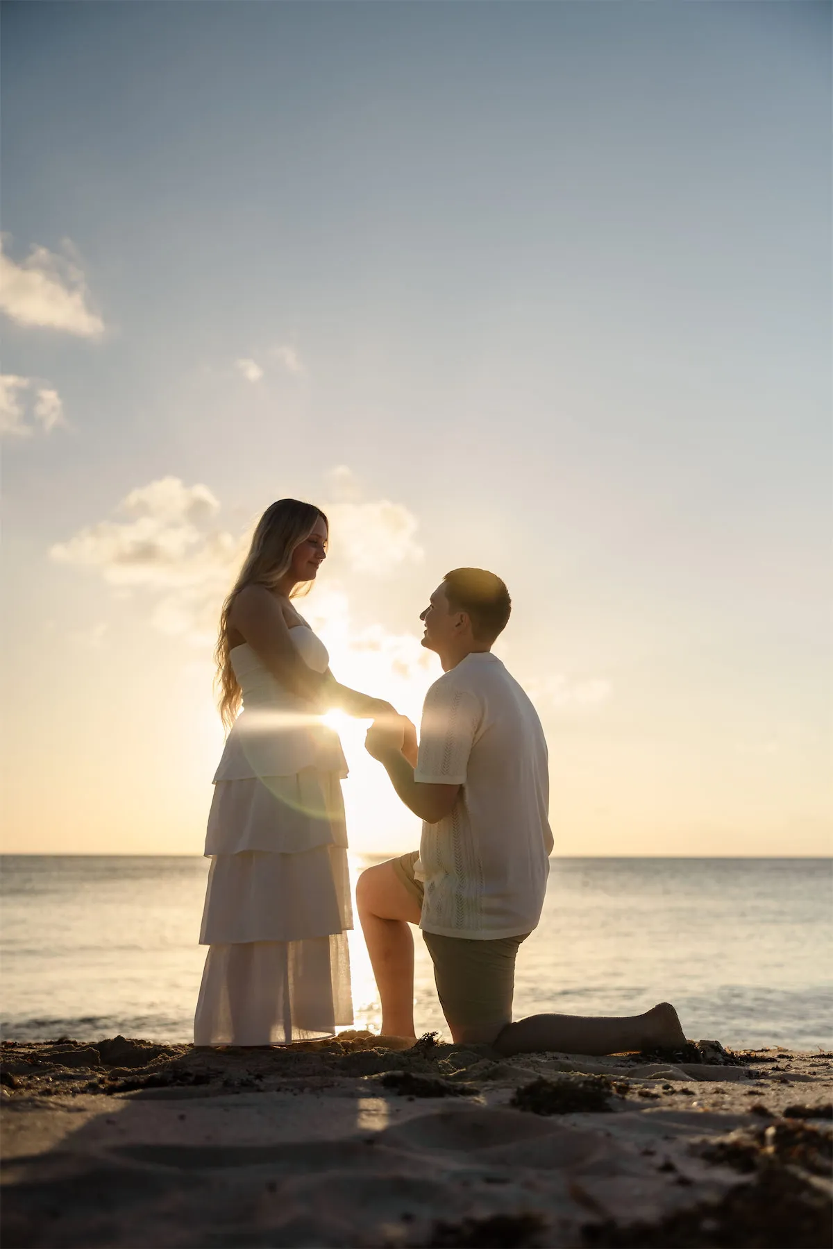 A man kneeling for a surprise proposal on a Cozumel beach at golden hour
