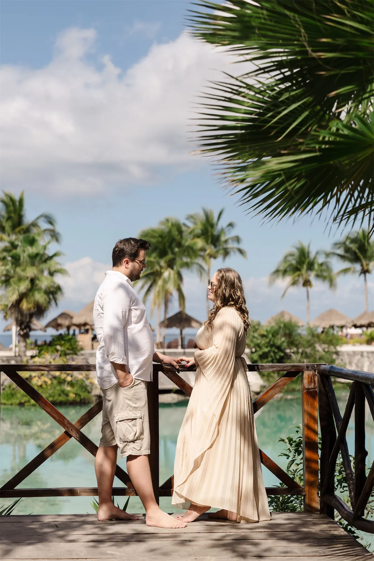 A couple posing on a wooden deck overlooking a beautiful tropical resort and lagoon in Cozumel.