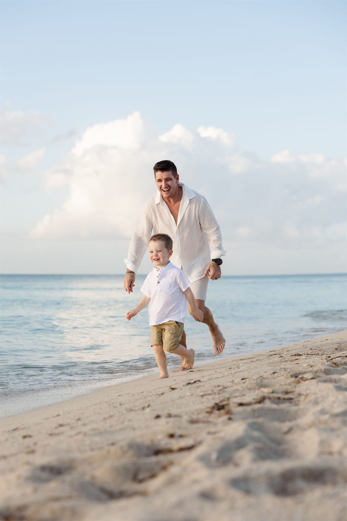 A father and young son laughing and running along the shoreline during a Cozumel beach photo session.