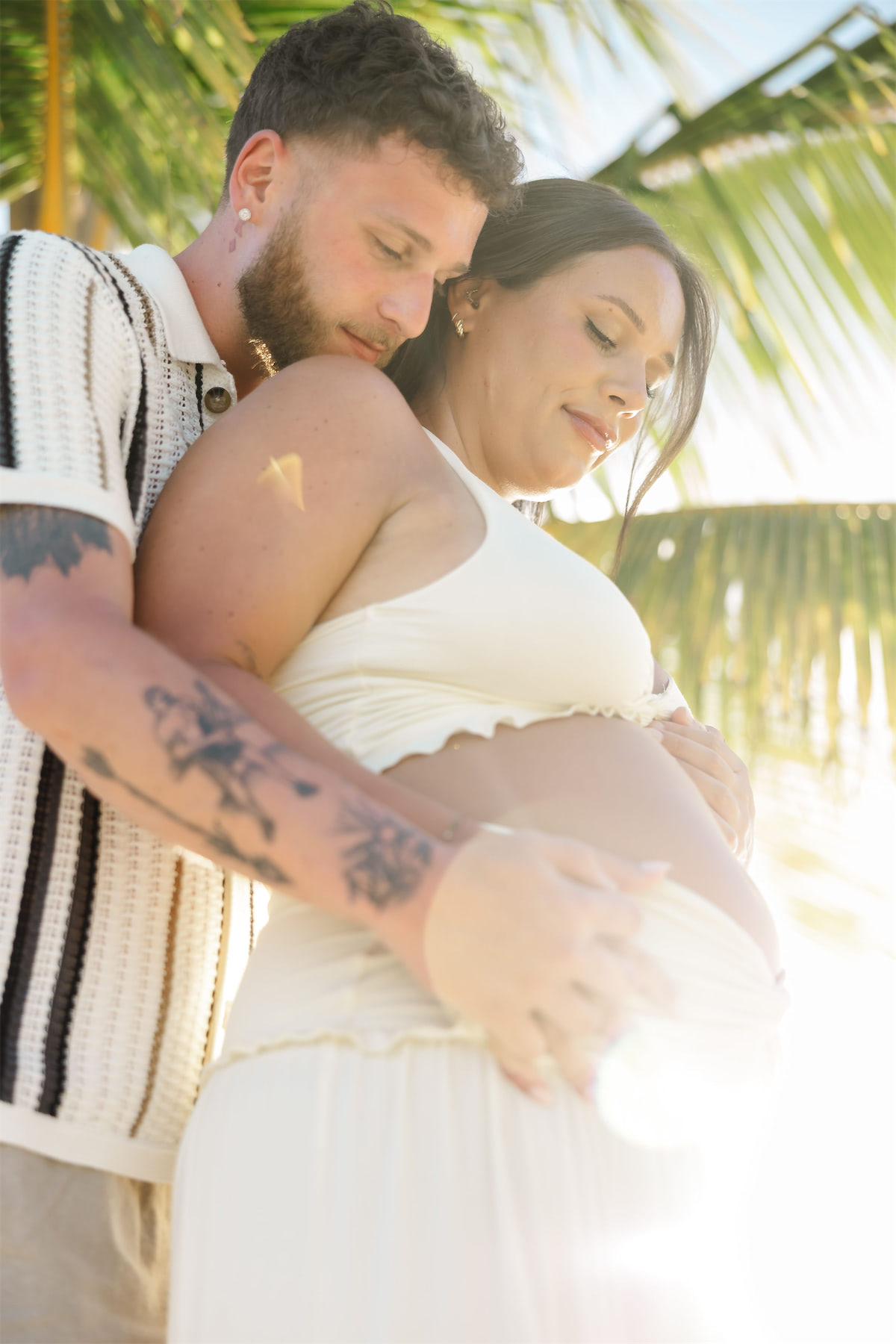 A man holding his partner's baby bump during a romantic maternity session on a Cozumel beach.